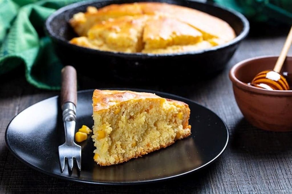 Sliced eggless cornbread with visible corn kernels and honey glaze in cast iron pan