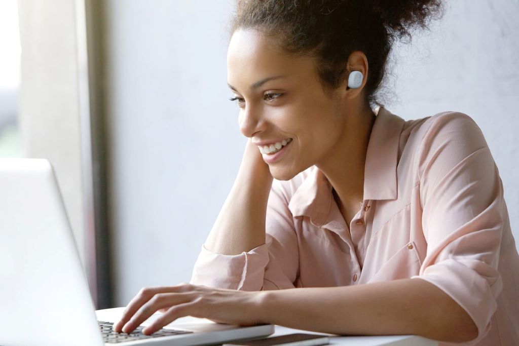 A person wearing modern wireless headphones while working on a laptop, seamlessly switching to answer a call on their smartphone