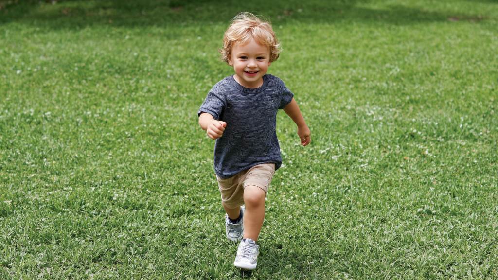 Toddler wearing Stride Rite wide sneakers running on grass happily