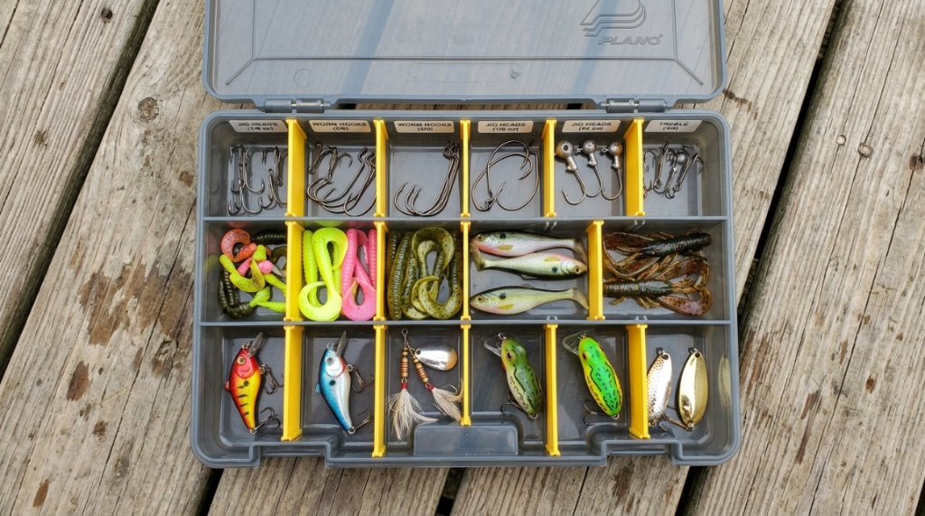 Clear plastic fishing lure organizers filled with colorful tackle on a wooden dock.